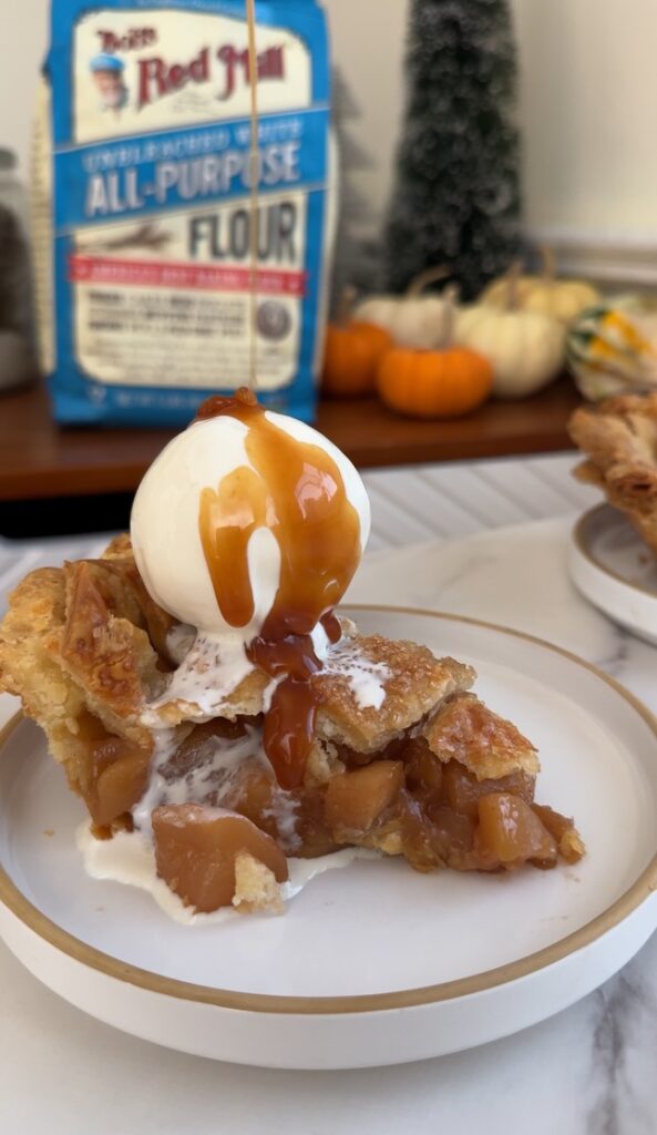 Salted Caramel Apple Pie topped with a scoop of vanilla ice cream and being drizzled with salted caramel sauce