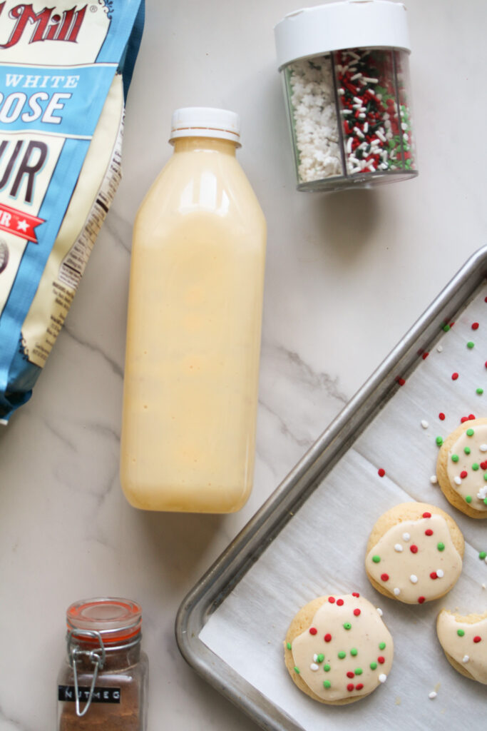 Eggnog sugar cookies on a sheet tray with a bottle of eggnog next to them