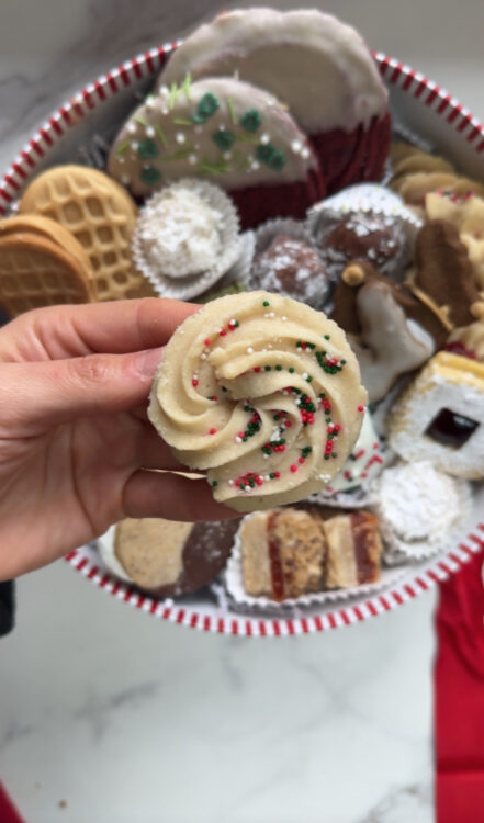 Classic Butter Cookie held in one hand with Christmas Cookie Box in the Background