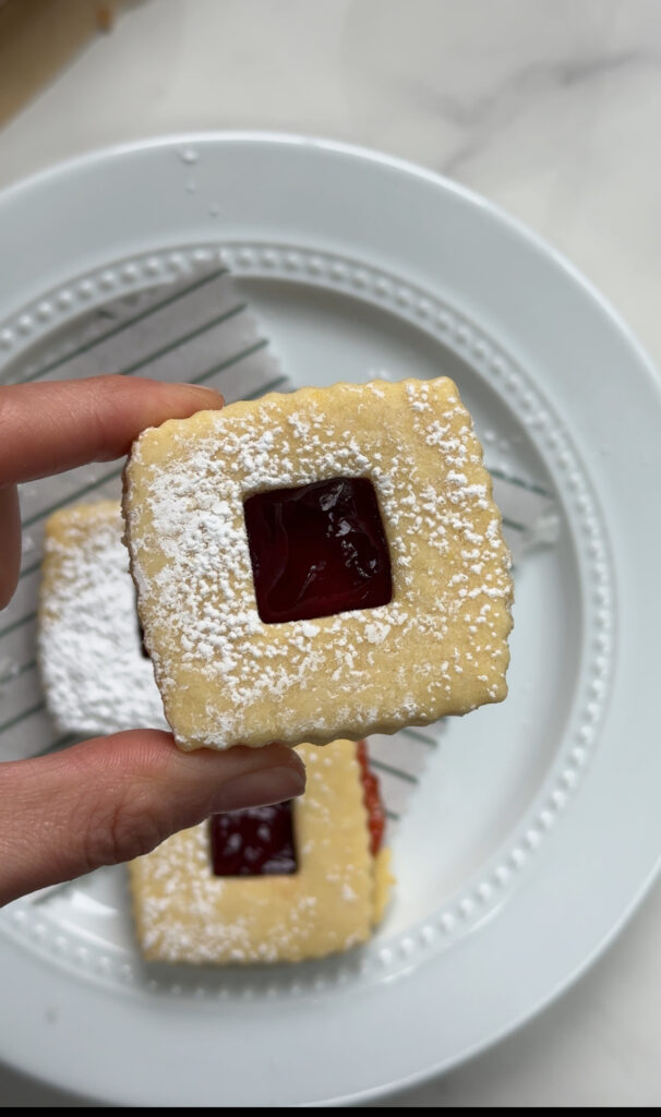 The Best Linzer Cookies Ever being held in one hand over a plate of linzer cookies