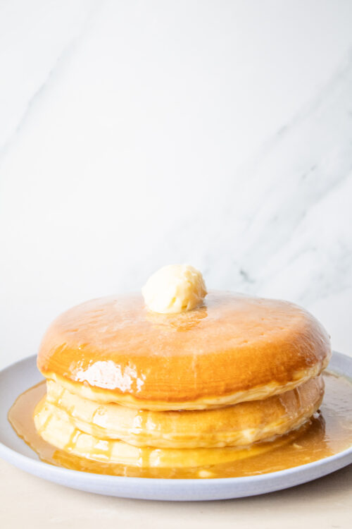 Golden Diner Pancakes stacked on a blue plate with honey butter syrup