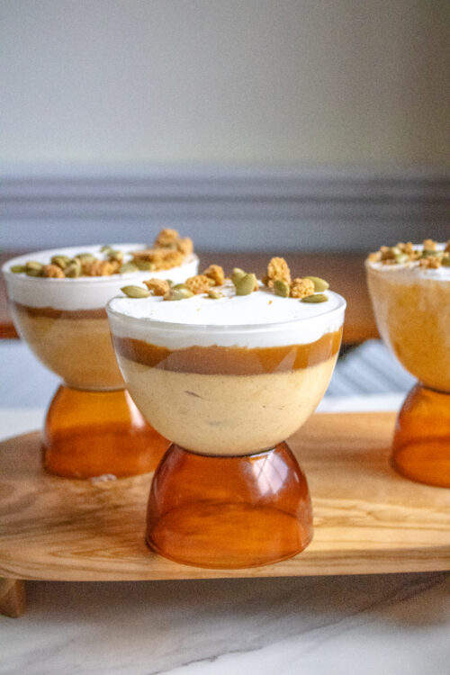 Pumpkin mousse in a coupe glass with salted caramel, whipped cream and gingersnap crumble and pepitas