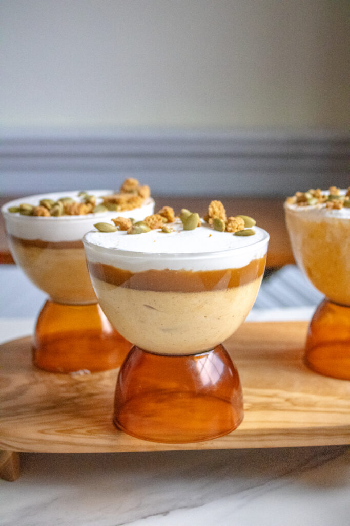 Pumpkin mousse in a coupe glass with salted caramel, whipped cream and gingersnap crumble and pepitas