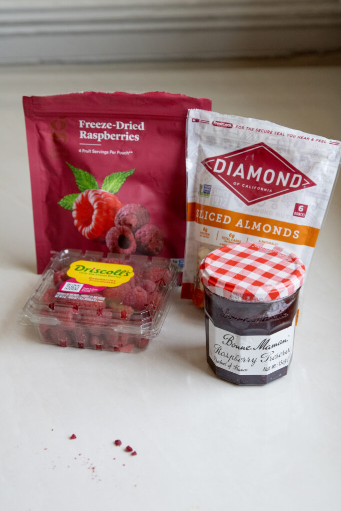 Freeze dried raspberries, sliced almonds, a container of raspberries, and Bonne Maman Raspberry Preserves